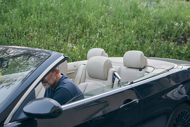 a contented middle-aged man sits in a convertible