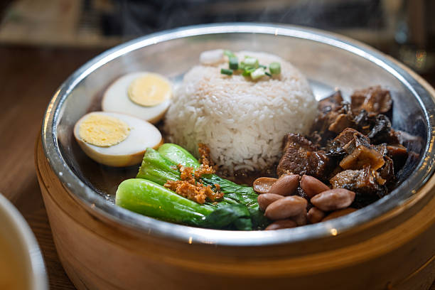 A hearty serving of braised pork with preserved vegetables, paired with steamed white rice, boiled egg, peanuts, and fresh greens. Served in a traditional metal bowl for an authentic dining experience.