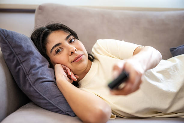 istock Young woman is holding remote control while watching television. 2213841457