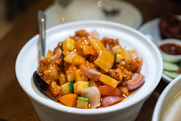 Sweet and sour pork with mixed vegetables, served in a white bowl. A vibrant mix of flavors and colors highlighting fresh ingredients and Asian cuisine.