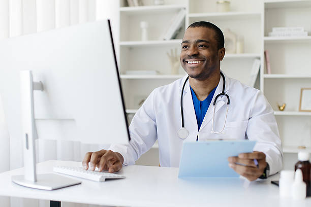 istock Smiling Black doctor working on computer while sitting at desk in office 2213841913