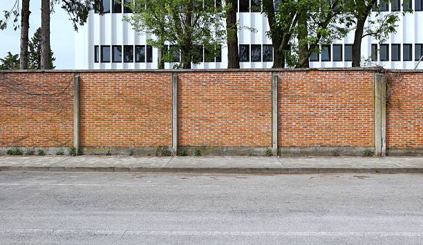 istock Surrounding brick wall with trees and white modern building on behind. Concrete sidewalk and  street in front 2213844880