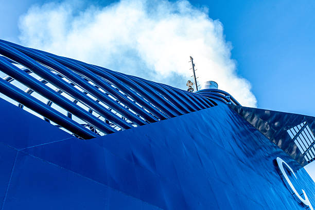 Barcelona, Catalonia - Spain - 01-10-2025: Diagonal view of the Grimaldi Cruise Roma ferry funnel with white smoke and parallel blue bars under a bright blue sky seen from below.