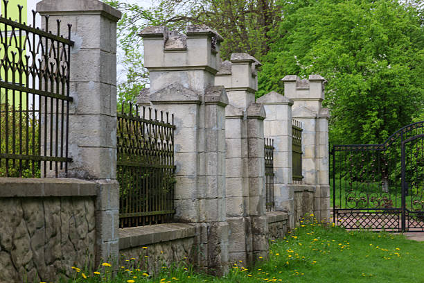 istock Stone fence with wrought iron elements and columns frames a green area with blooming yellow dandelions in the foreground. Spring day in the park. 2213848106