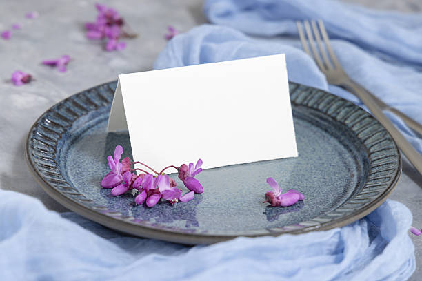 Wedding table place with folded card near wild purple flowers and fabric closeup, mockup Pastel wedding table place with an folded card on plate near wild purple flowers and light blue fabric closeup. Name card mockup for spring party design or romantic wedding stationery light blue silk stock pictures, royalty-free photos & images