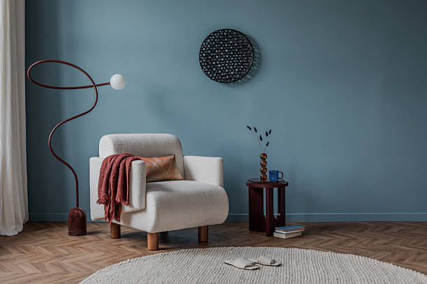 istock Cozy reading nook with a curved white armchair, warm rust-toned textiles, and a sleek sculptural floor lamp. 2213851027