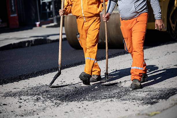 istock Workers in orange uniforms repair road surface with shovels at construction site during daylight hours 2213853272