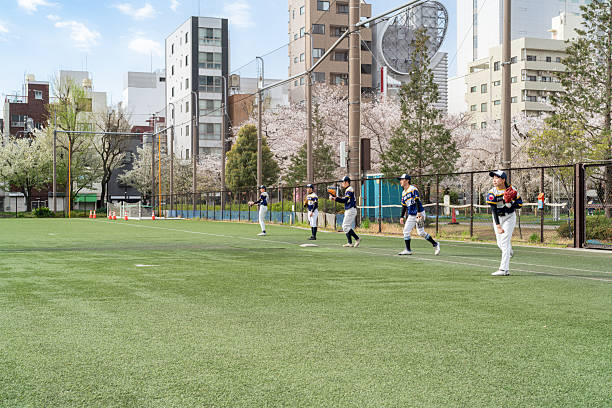 A local baseball team practices in Tokyo, showcasing teamwork, community, and friendship during a pleasant spring day. The scene captures the essence of sports and urban outdoor activity.