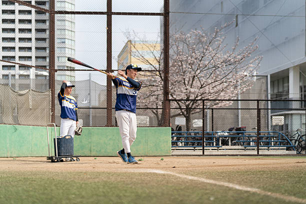 istock Two Baseball Players Practicing in a Local Park With Spring Cherry Blossoms Nearby 2213856403