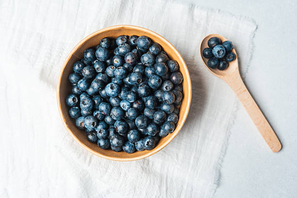 istock Fresh blueberries in wooden bowl on light fabric background 2213856958