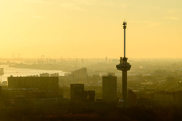 Euromast Rotterdam sunset skyline from a height view at the New Maas. In the far distance the port of Rotterdam is visible on the horizon. The Euromast on the right, standing at 185 meters  tall, it was originally built in 1960, designed by architect Huig Maaskant and engineer G. J. de Haan, and it remains one of the tallest structures in the city of Rotterdam.