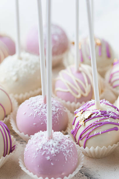 istock Assortment of violet cakepops with pearls and different chocolate decoration on a white marble background. Cake pops with shiny sprinkles 2213860909