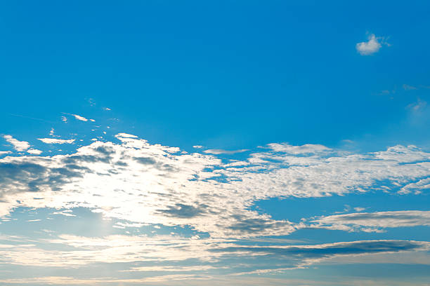 Bright blue sky filled with scattered, fluffy white clouds, illuminated by soft sunlight. Scene is calm and expansive, with a small, wispy cloud near top left adding a subtle contrast to vibrant sky