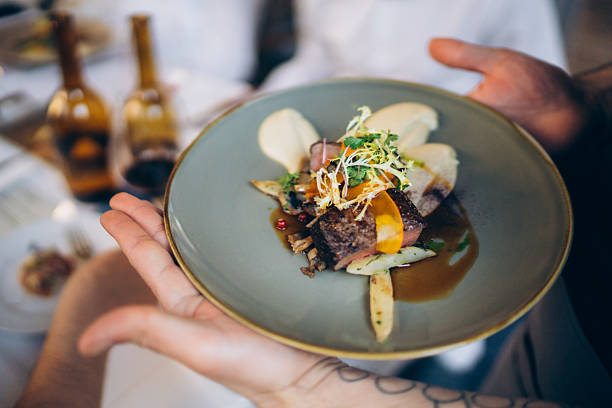 A beautifully arranged gourmet beef dish features tender meat, garnished with fresh vegetables and a colorful sauce. It is being served in a fine dining setting during a special occasion.