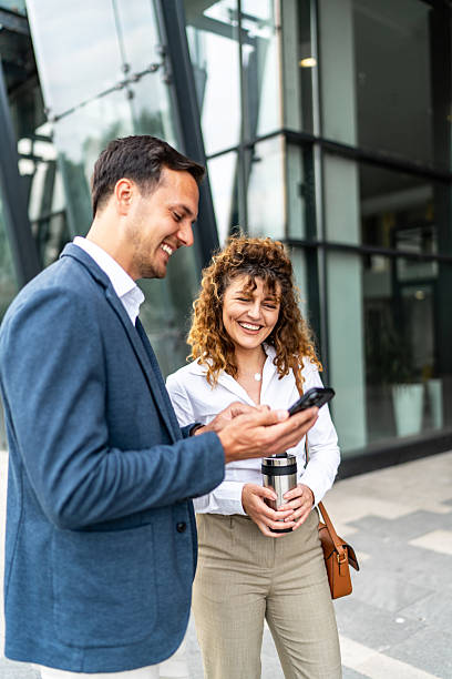 istock Businesspeople smiling and using smartphone outside office building 2213873613