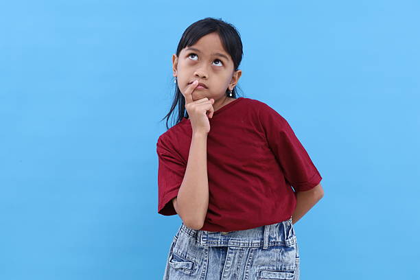 Adorable asian little girl standing while thinking something. Isolated on blue with copyspace