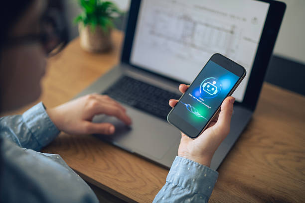 Close-up of woman in business uses AI chatbot on mobile while working on computer