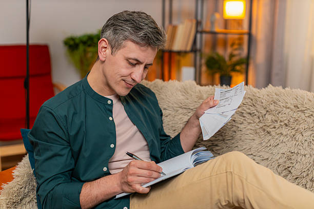 istock Man manages household budget writing numbers in notebook checking bills with serious focused look 2213886055