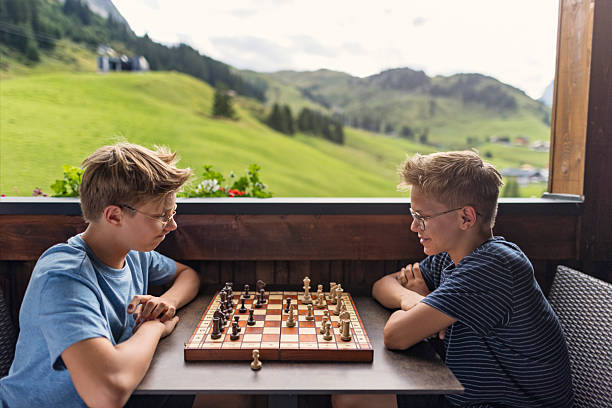 Two people are engaged in a thoughtful chess game on a wooden deck or patio with a breathtaking view of rolling green hills and distant mountains. The atmosphere is calm and picturesque, creating a perfect setting for concentration and friendly competition. Shot with Canon R5