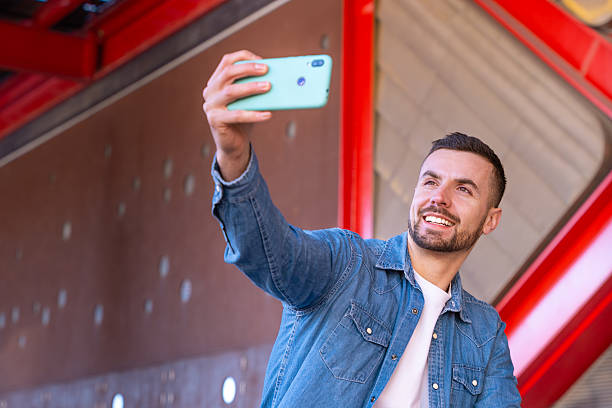 istock Smiling young man taking selfie with smartphone in urban setting with red beams 2213896271