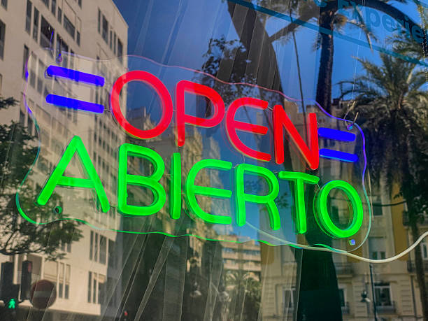 Low angle close-up view of an illuminated open neon sign in store window with reflection of the city of Valencia on it, Spain