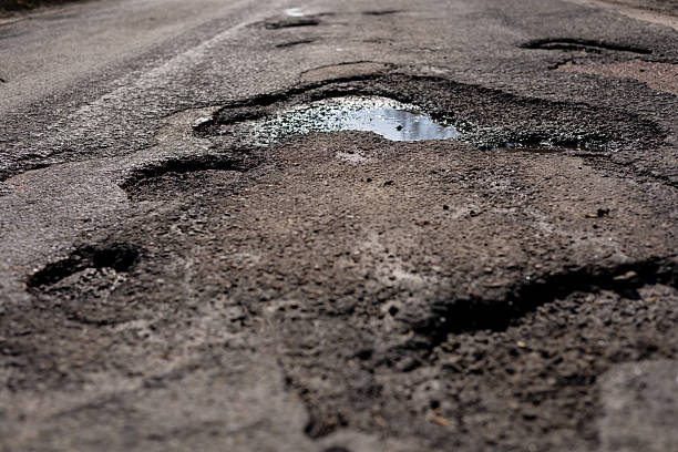 istock Deep potholes create obstacles on a rural road, with rainwater pooling in one of them on a cloudy day during early spring 2213902154