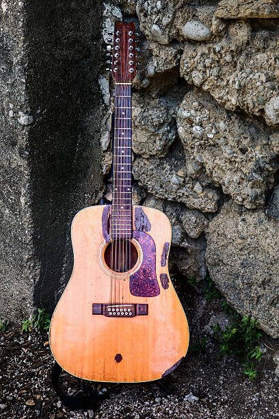 istock Old acoustic guitar stands against a rugged stone wall in a rustic outdoor setting during daylight hours 2213903635