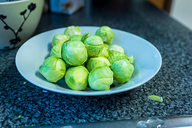 Fresh raw brussels sprouts on plate on dark kitchen tabletop.