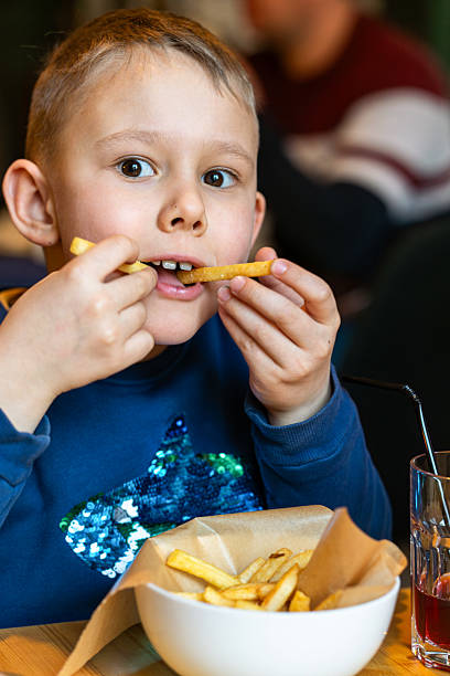 istock Smiling boy playfully biting French fry while enjoying meal in restaurant settings 2213904899