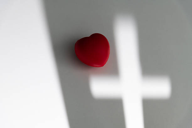 Religious cross shadow and red heart on white background