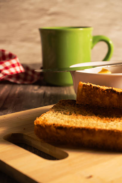 Toasted slices of bread on a wooden cutting board, with butter and coffee ready for breakfast