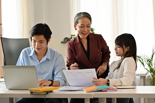 istock Confident senior executive guiding two young team members, Business teamwork, mentorship, and intergenerational collaboration in a professional workplace setting 2213911276
