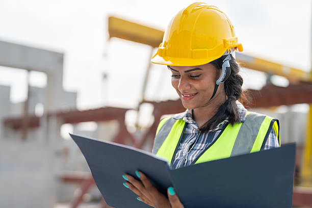 istock Asian woman engineer holding document smiling at construction site. Confident female Indian wearing protective helmet and vest working in factory making precast concrete wall for real estate housing. 2213912301