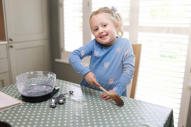 istock Four year old girl sat quietly at a kitchen table in a domestic kitchen waiting for her grandmother to make a cake 2213916897