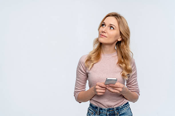 istock Caucasian woman holding mobile phone looking up on copy space your logo advertisement doing ecommerce online shopping on cell, using trendy apps isolated over white background 2213920919