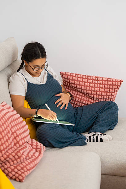 istock Pregnant woman relaxing on sofa and drawing on tablet 2213923727