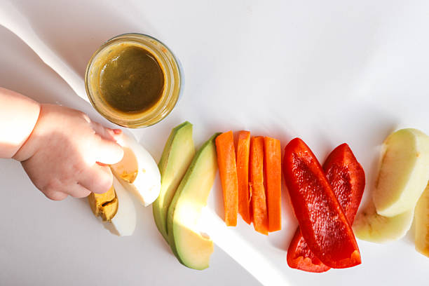 istock A child's hands reaching for freshly chopped vegetables on a white surface. Includes diced avocado, carrot, apple slices, bell pepper, and tomato pieces. Minimalist food composition. 2213924471