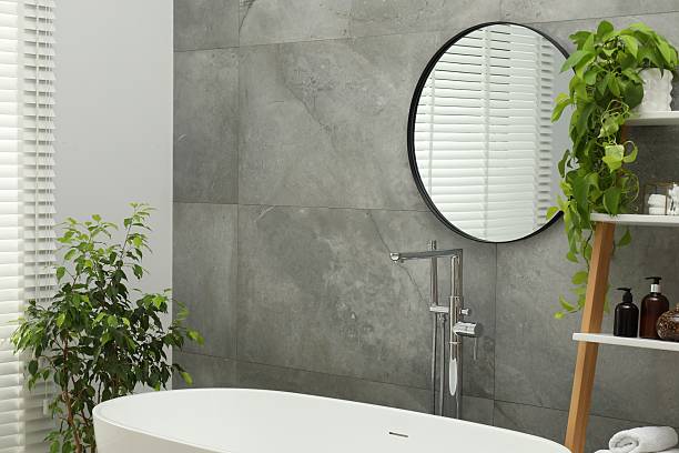 istock Round mirror on grey tiled wall over tub in bathroom 2213925349