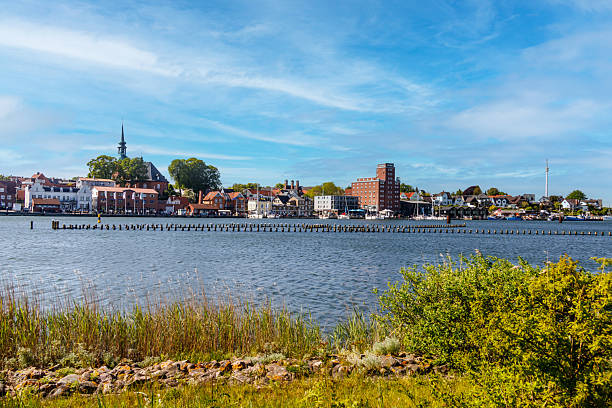 Cityscape of Kappeln, germany, with colorful buildings, church tower and harbor reflecting on the calm water of the river schlei under a blue sky