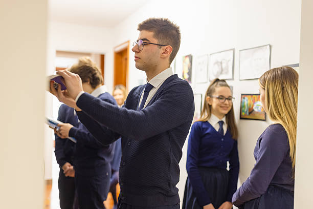 A group of high school students in uniform, interacting and taking photos in a school hallway.