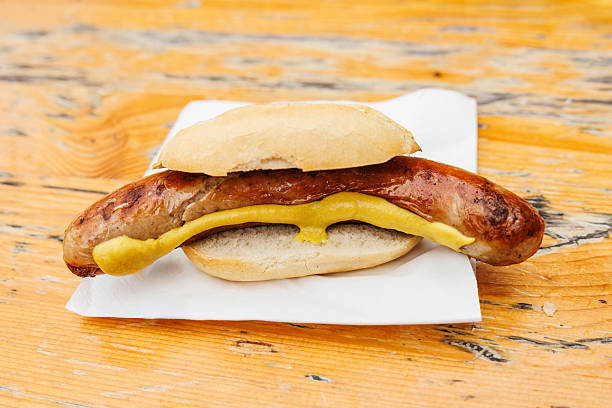 Juicy german Brtwurst sausage with mustard served in a bun on a wooden surface.