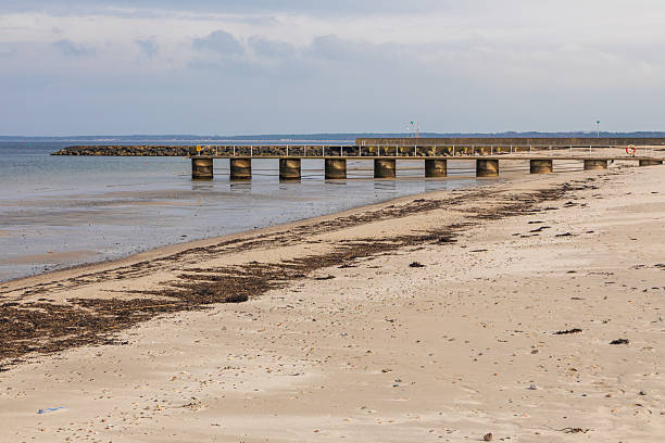 Concrete pier stretching into the sea with sandy beach in Torekov, Sweden. Overcast weather and low tide.