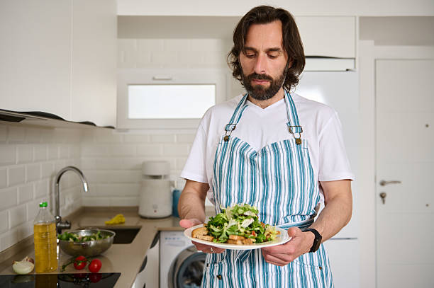 istock Man Wearing Apron Preparing a Healthy Salad in Modern Light Kitchen 2213947400