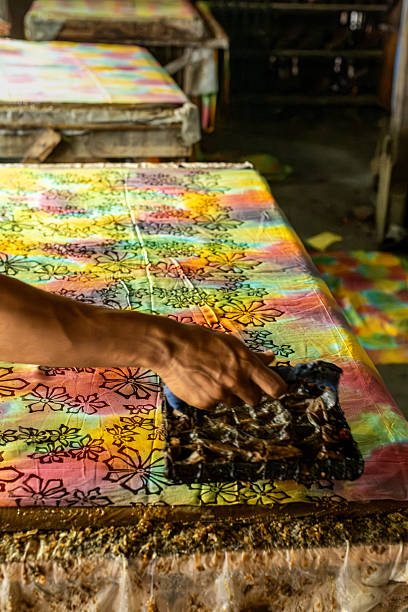 Artisan applying dye to a batik fabric with traditional tool