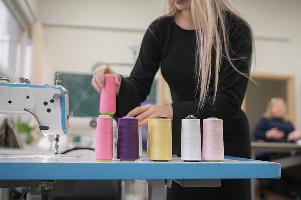 Seamstress organizes vibrant thread rolls on a table while working at a sewing machine in a well-lit crafting space.