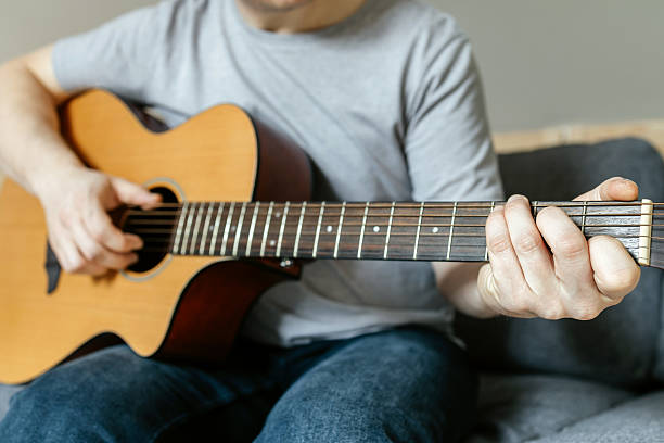 istock Man sitting and playing guitar, strumming chords, learning to play. Hobbies for adults 2213951334