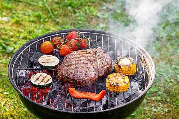 beef steak meat and vegetables cooking on hot charcoal grill in garden