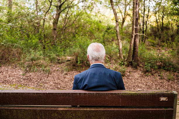 Mature adult man enjoys a peaceful moment sitting on a bench surrounded by lush green trees in the park