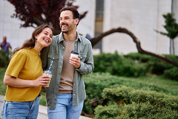 istock Happy couple laughing and walking together while drinking coffee 2213958905