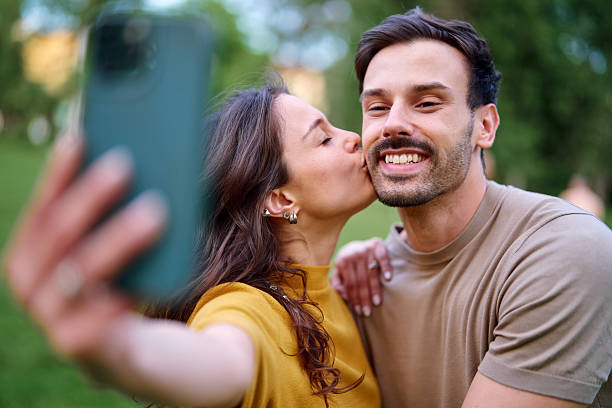 istock Young couple taking a selfie while kissing in a park 2213959808